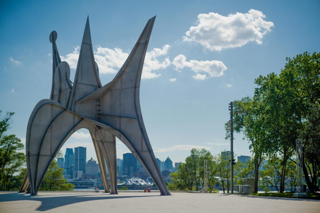 Dramatic stainless steel sculpture in a Montreal park with city skyline view.